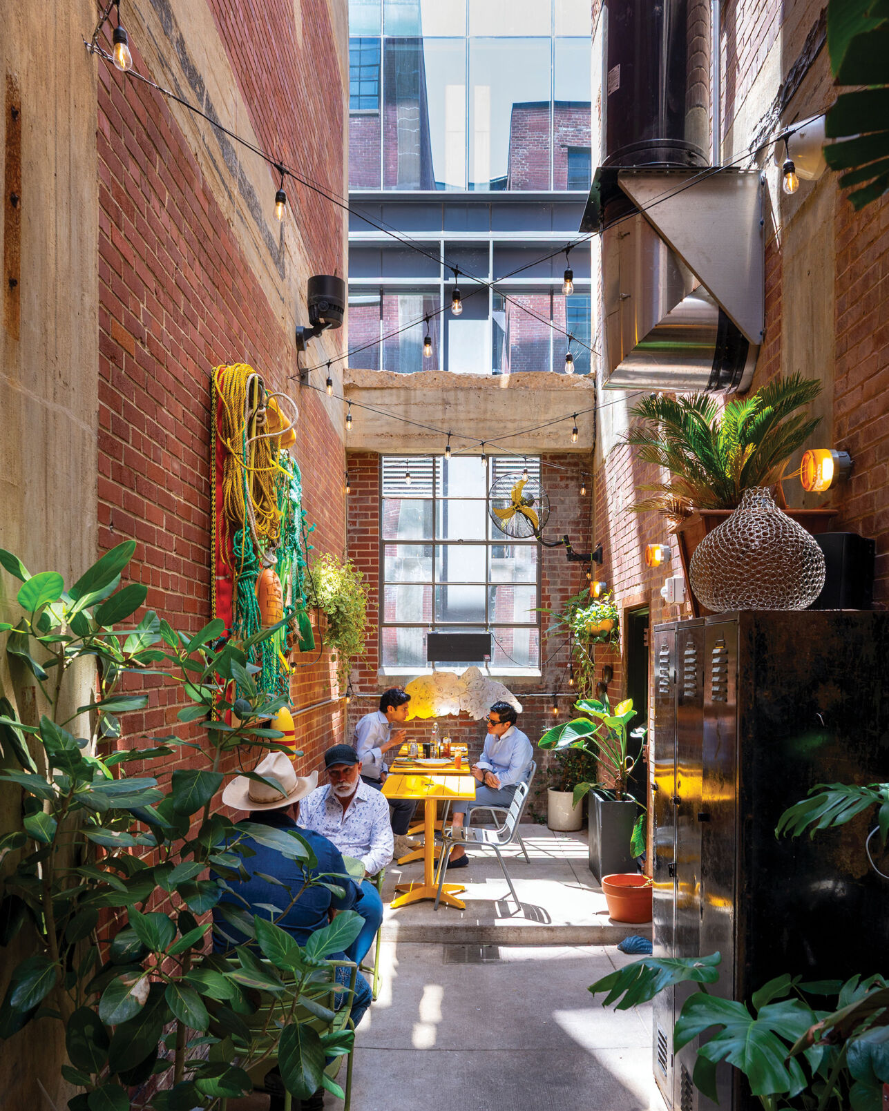 Diners sit at tables in a narrow brick corridor with high ceilings near some lockers